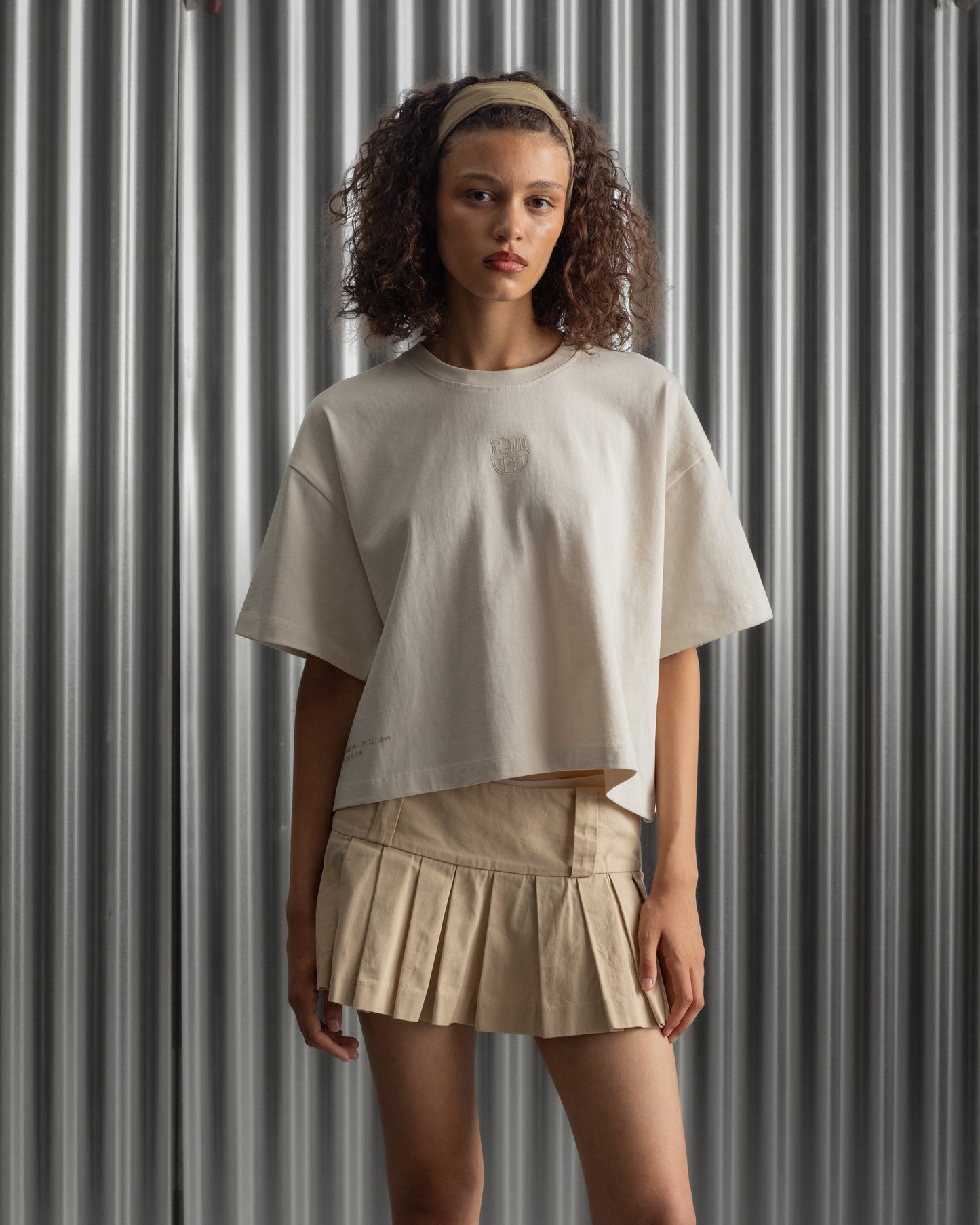 Beige cropped FC Barcelona t-shirt, back view, with gold FCB logo and the phrase “Good Game Lover’s Crew since 1899” printed in black above it.