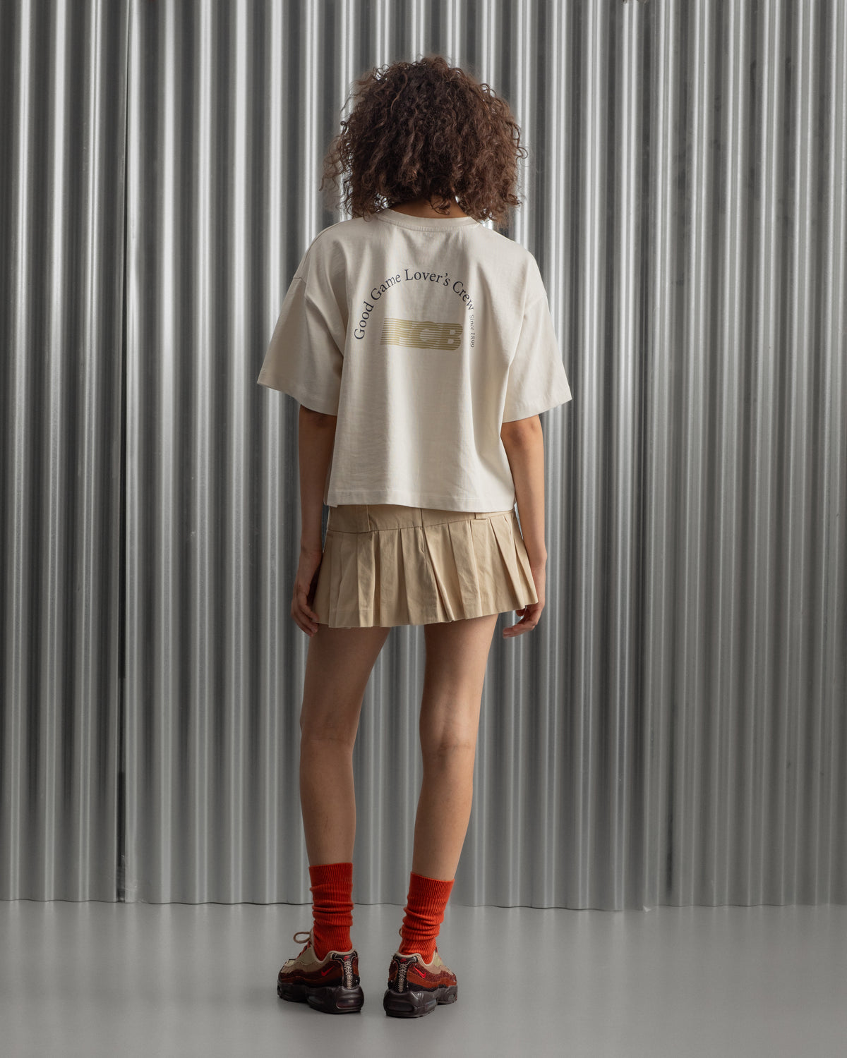 Beige cropped FC Barcelona t-shirt, back view, with gold FCB logo and the phrase “Good Game Lover’s Crew since 1899” printed in black above it.