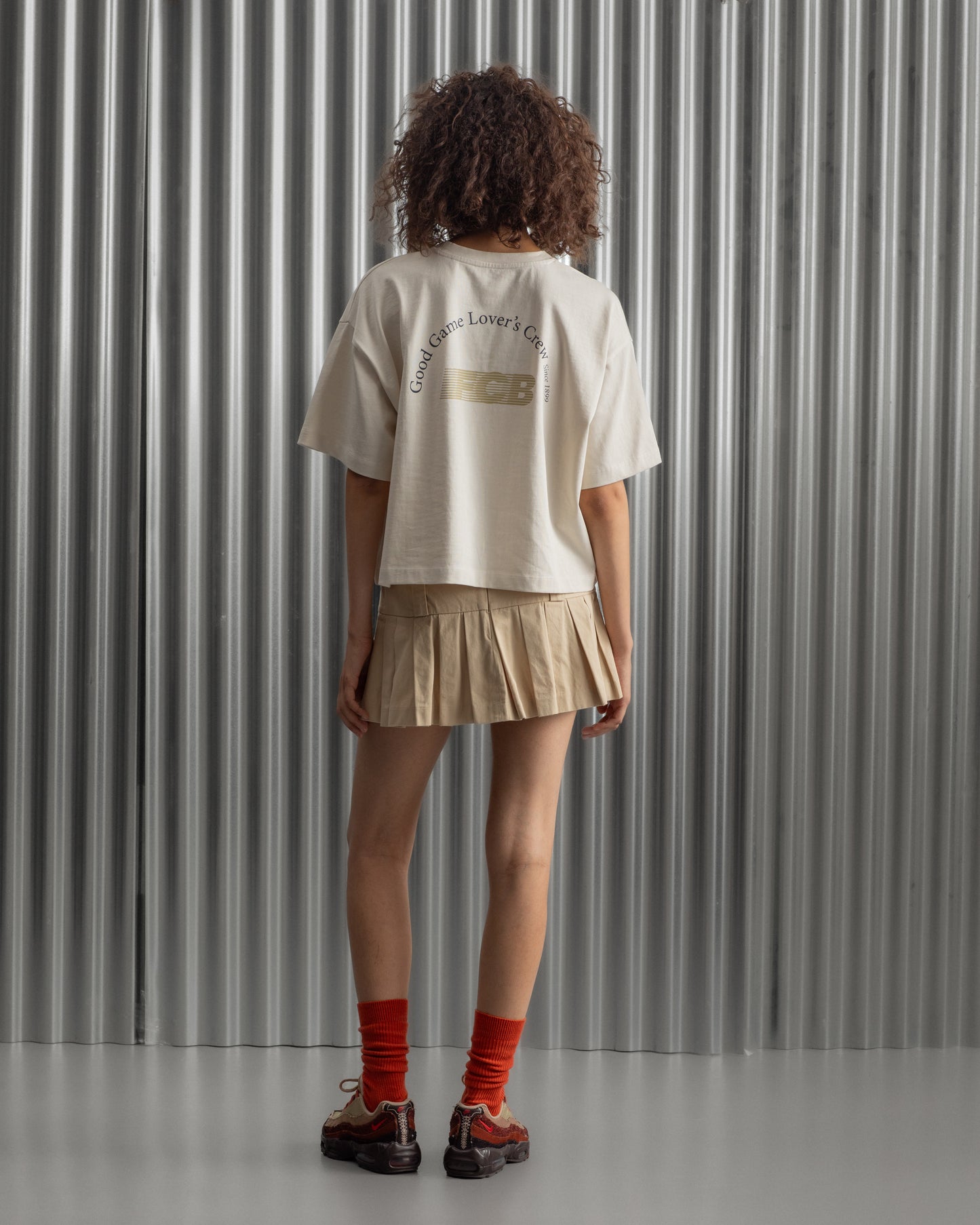 Beige cropped FC Barcelona t-shirt, back view, with gold FCB logo and the phrase “Good Game Lover’s Crew since 1899” printed in black above it.