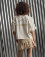 Beige cropped FC Barcelona t-shirt, back view, with gold FCB logo and the phrase “Good Game Lover’s Crew since 1899” printed in black above it.