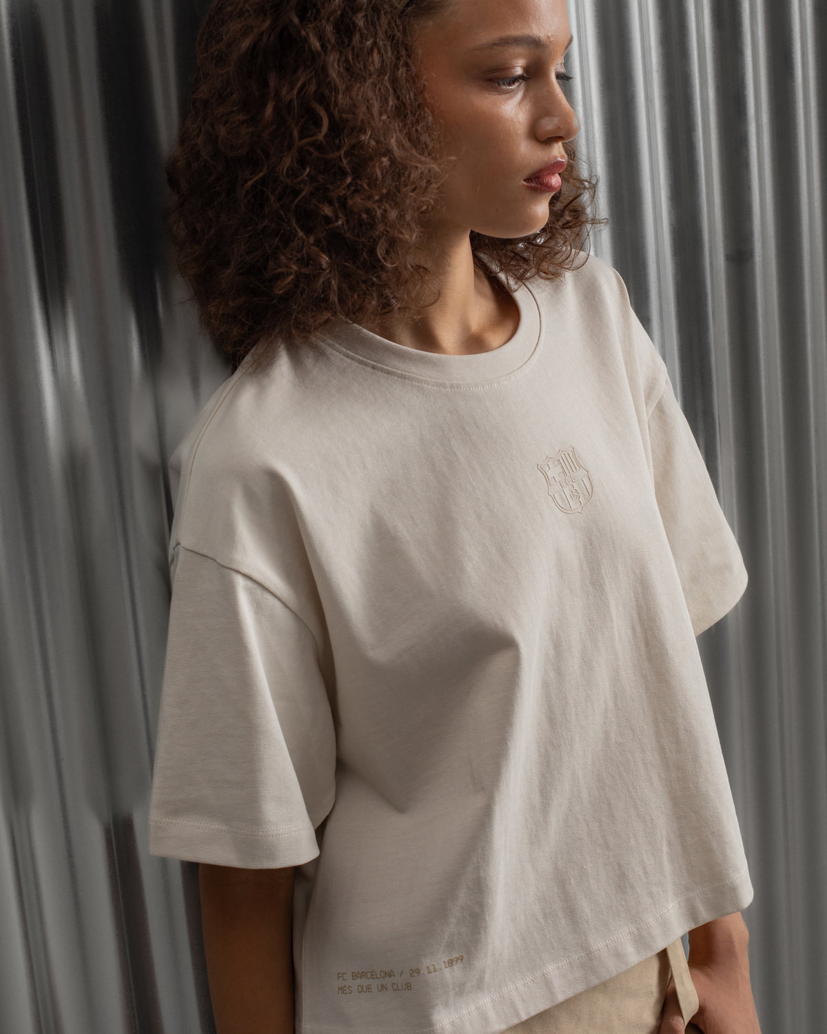 Beige cropped FC Barcelona t-shirt, back view, with gold FCB logo and the phrase “Good Game Lover’s Crew since 1899” printed in black above it.