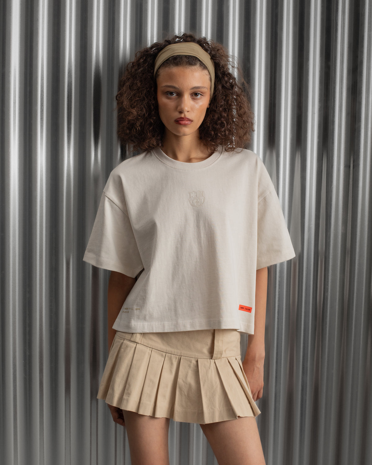 Beige cropped FC Barcelona t-shirt, back view, with gold FCB logo and the phrase “Good Game Lover’s Crew since 1899” printed in black above it.