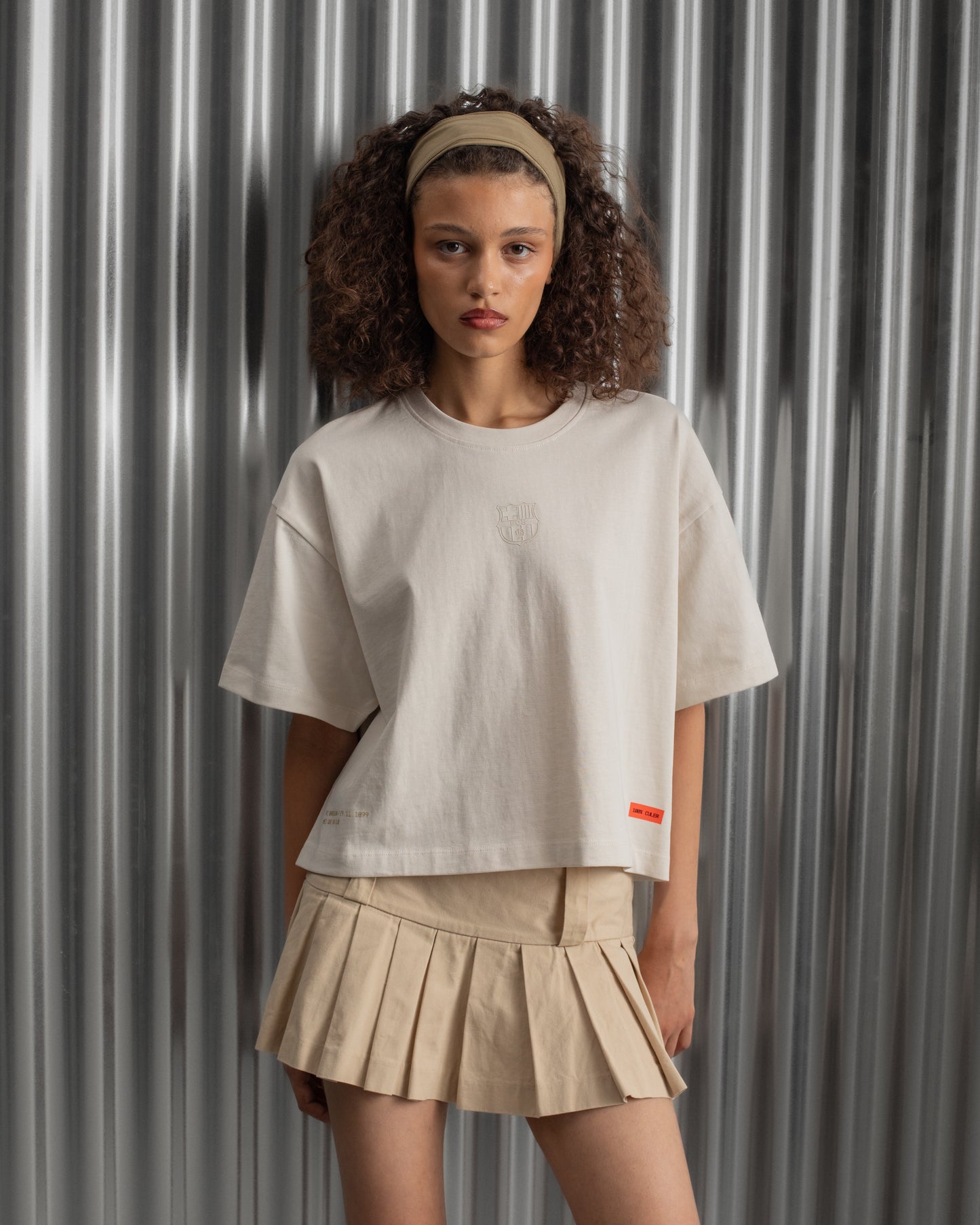 Beige cropped FC Barcelona t-shirt, back view, with gold FCB logo and the phrase “Good Game Lover’s Crew since 1899” printed in black above it.