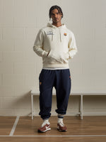 Man facing the camera wearing a cream hoodie with bold 'Fan Club Barcelona' text on the back, paired with navy shorts.