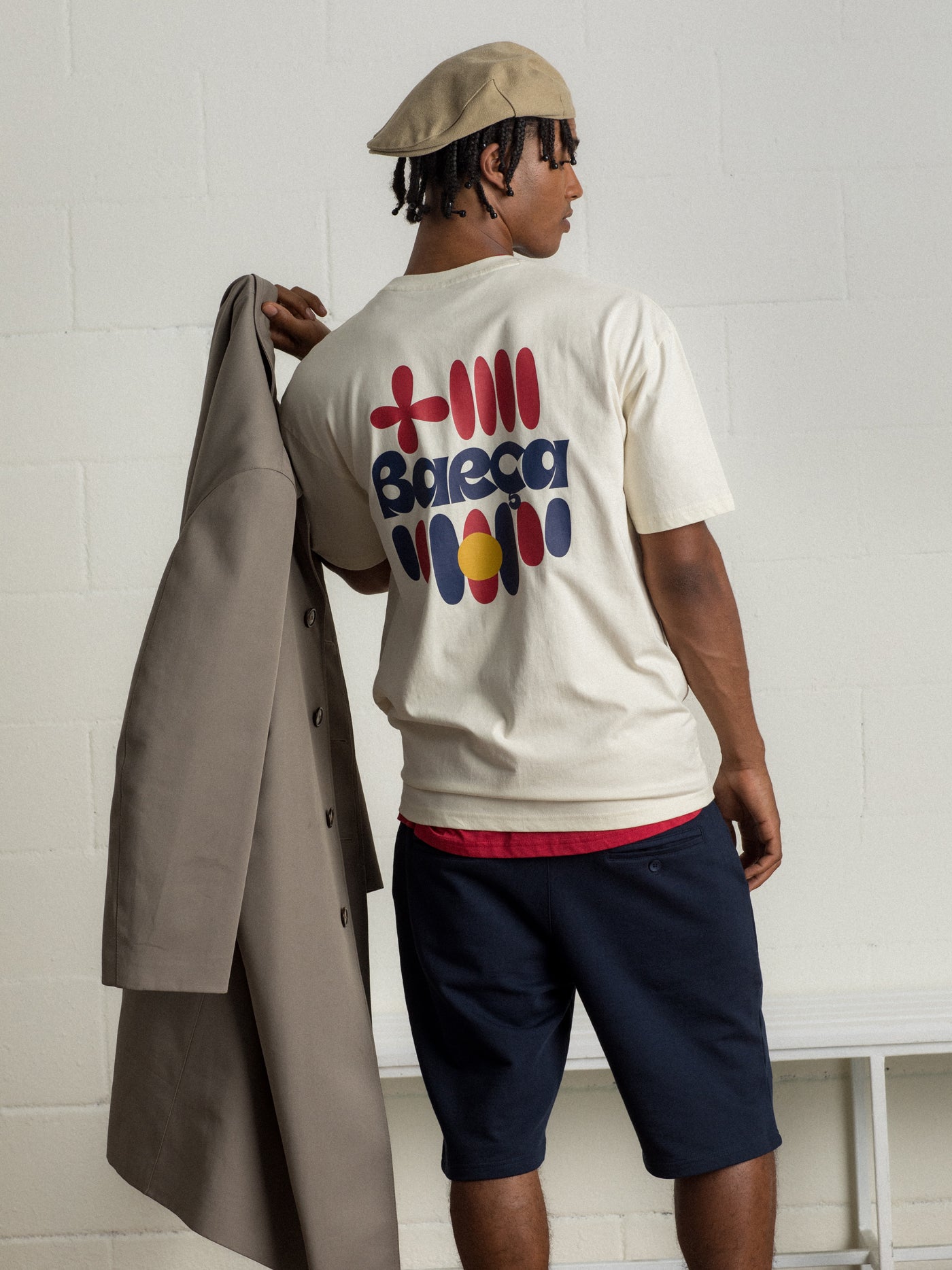 "Man wearing a beige beret and cream-colored T-shirt with FC Barcelona crest and 'Fan Club Barcelona' text, holding a light jacket over his shoulder."

