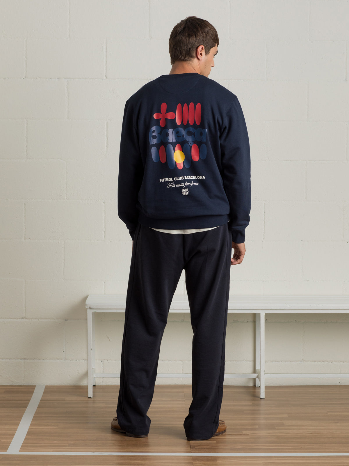 Man wearing a navy sweatshirt with a colorful abstract Barça design and 'Futbol Club Barcelona' text on the back