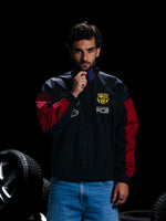 Man wearing a sports jacket with a logo, standing next to car tires on a dark background