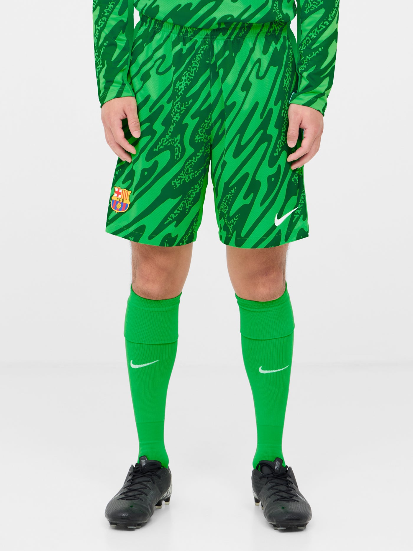Person wearing green FC Barcelona goalkeeper shorts with abstract pattern, Nike logo, and club crest.

