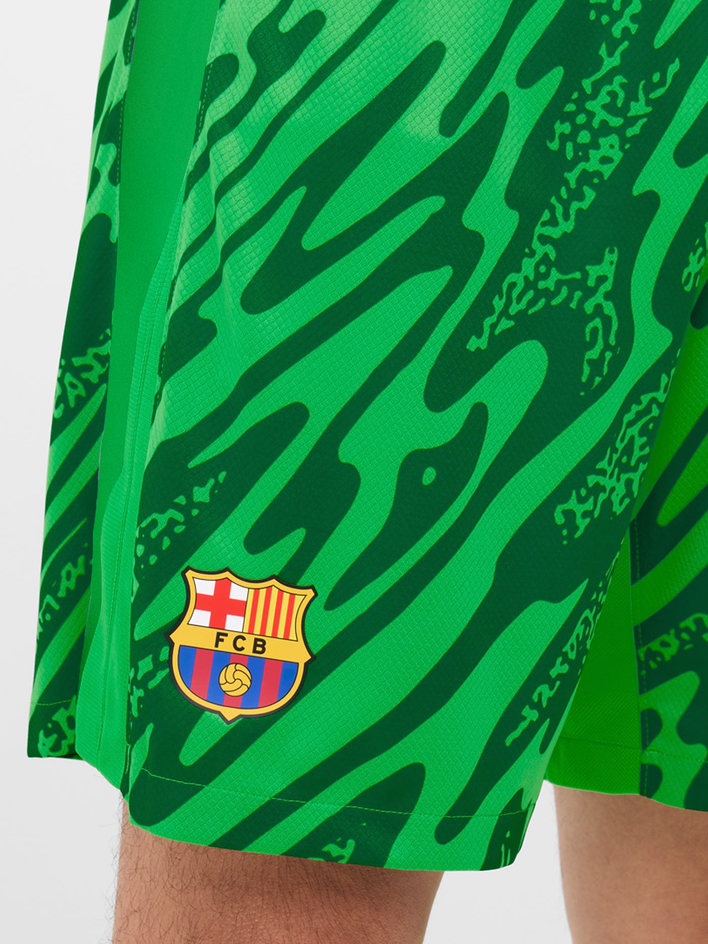 Person wearing green FC Barcelona goalkeeper shorts with abstract pattern, Nike logo, and club crest.