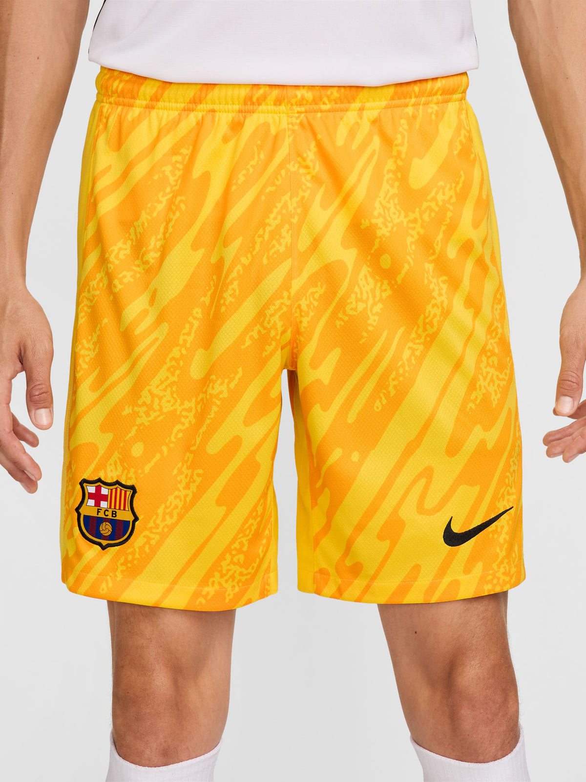 Person wearing bright yellow FC Barcelona goalkeeper shorts with abstract pattern, Nike logo, and club crest.