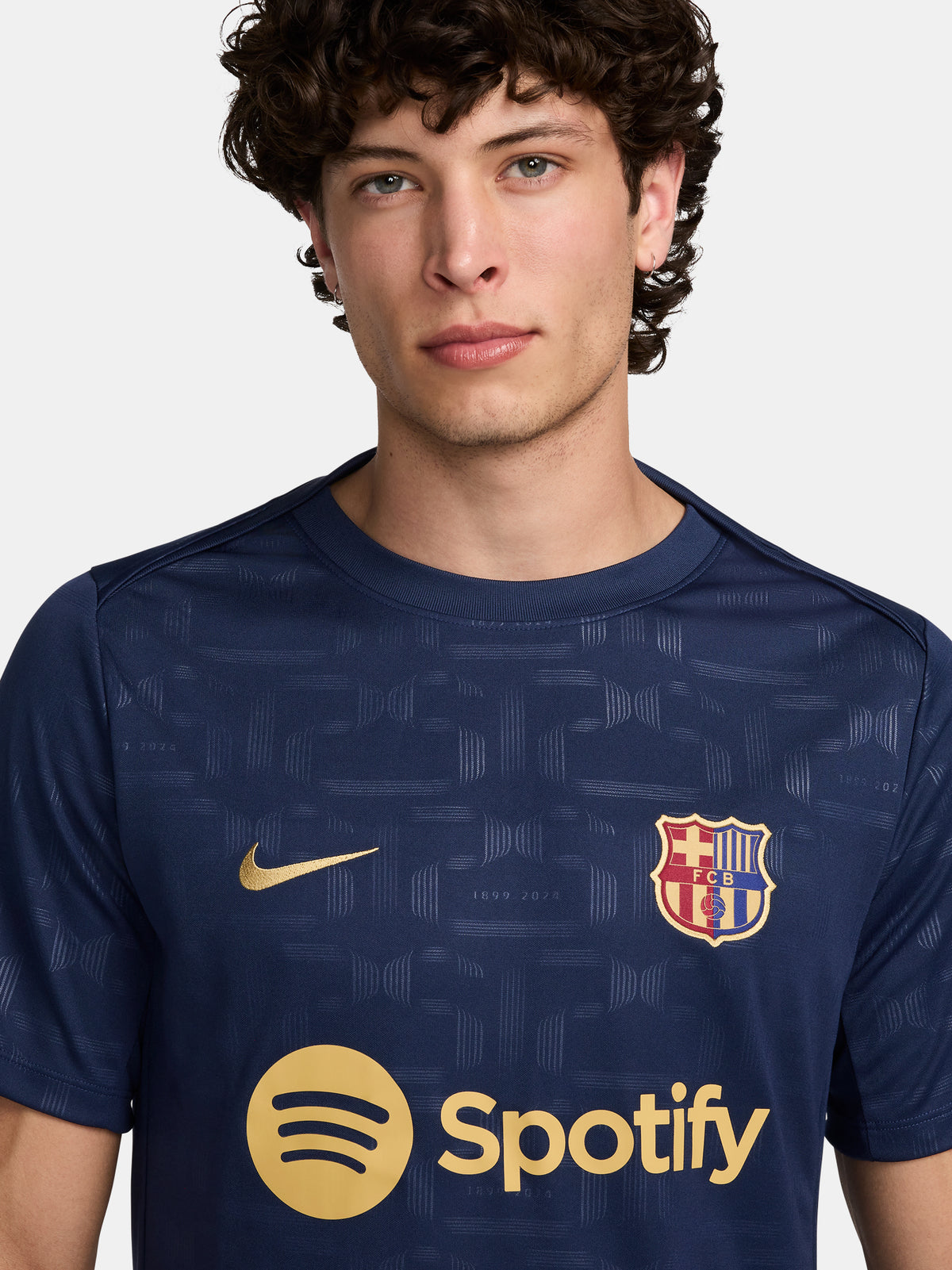 FC Barcelona training shirt in dark navy blue featuring subtle tonal geometric patterns. The shirt displays a golden Nike swoosh on the right chest, the FC Barcelona crest on the left chest, and a bold gold Spotify logo centered across the front.