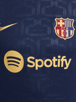 FC Barcelona warm-up shirt featuring a black base with a striking vertical stripe pattern in alternating red and blue. The shirt displays the red Spotify logo in the center, along with the Nike swoosh and FC Barcelona crest, also in red.