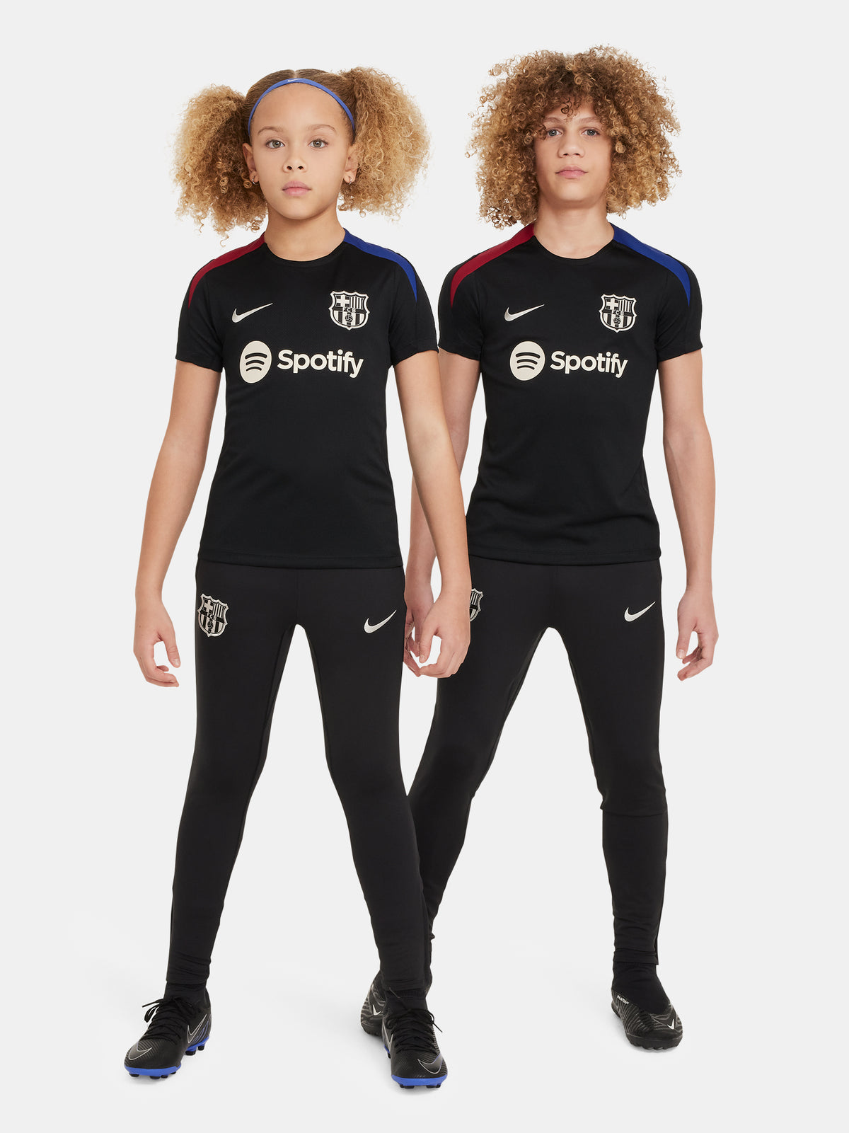 FC Barcelona black kids' training shirt with white Spotify logo and crest, red and blue shoulder details.
