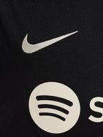 FC Barcelona black kids' training shirt with white Spotify logo and crest, red and blue shoulder details.