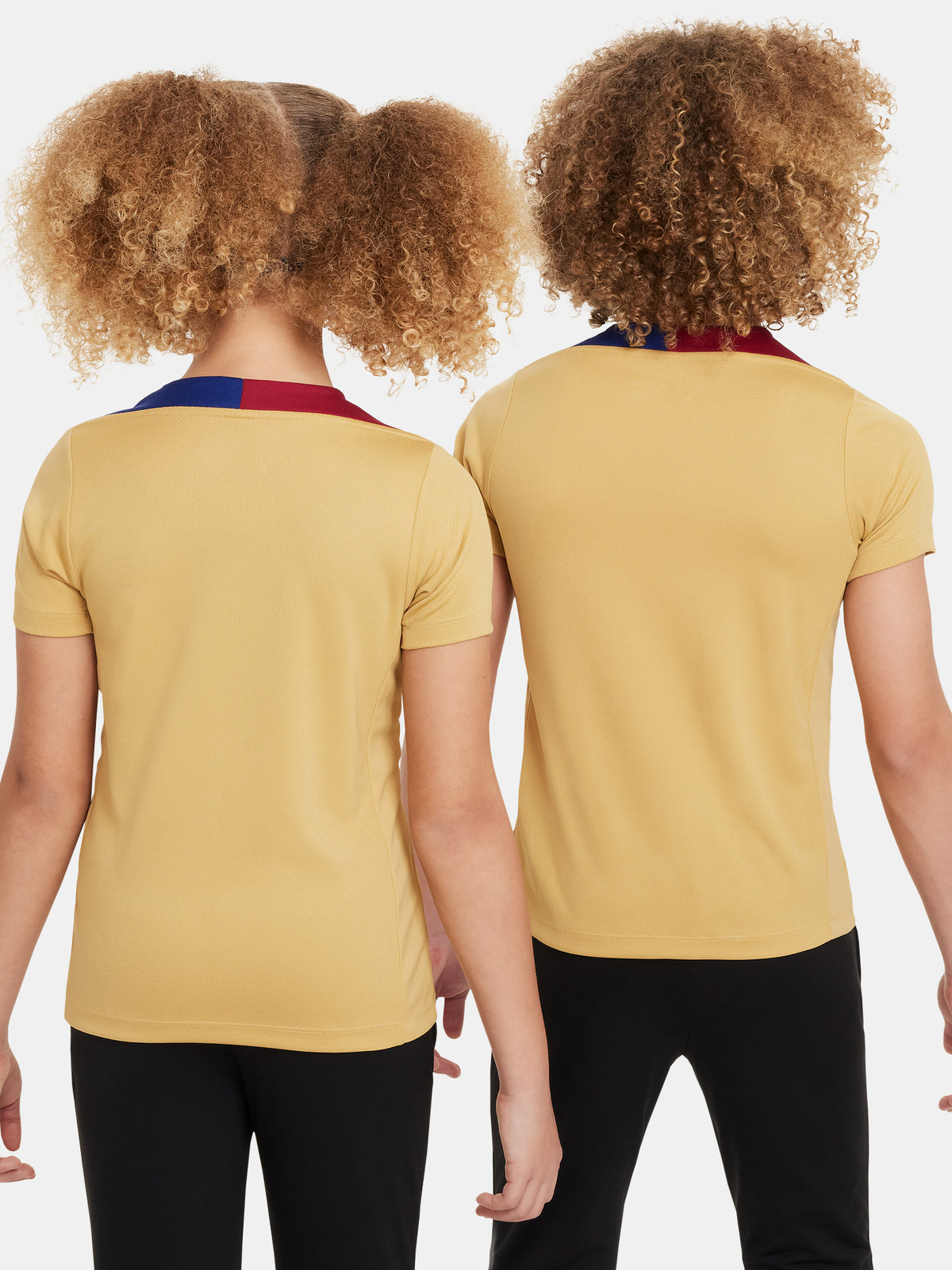 Two children wearing FC Barcelona gold training kits with short sleeves, featuring red and blue shoulder stripes, Nike logos, and Spotify sponsor branding.