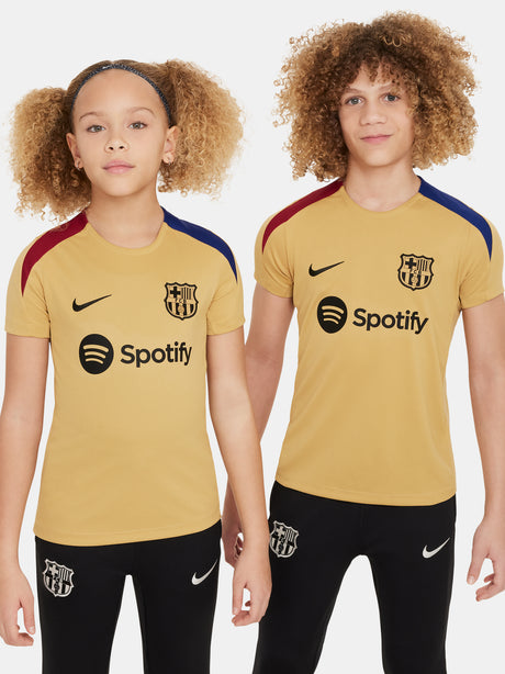 Two children wearing FC Barcelona gold training kits with short sleeves, featuring red and blue shoulder stripes, Nike logos, and Spotify sponsor branding.