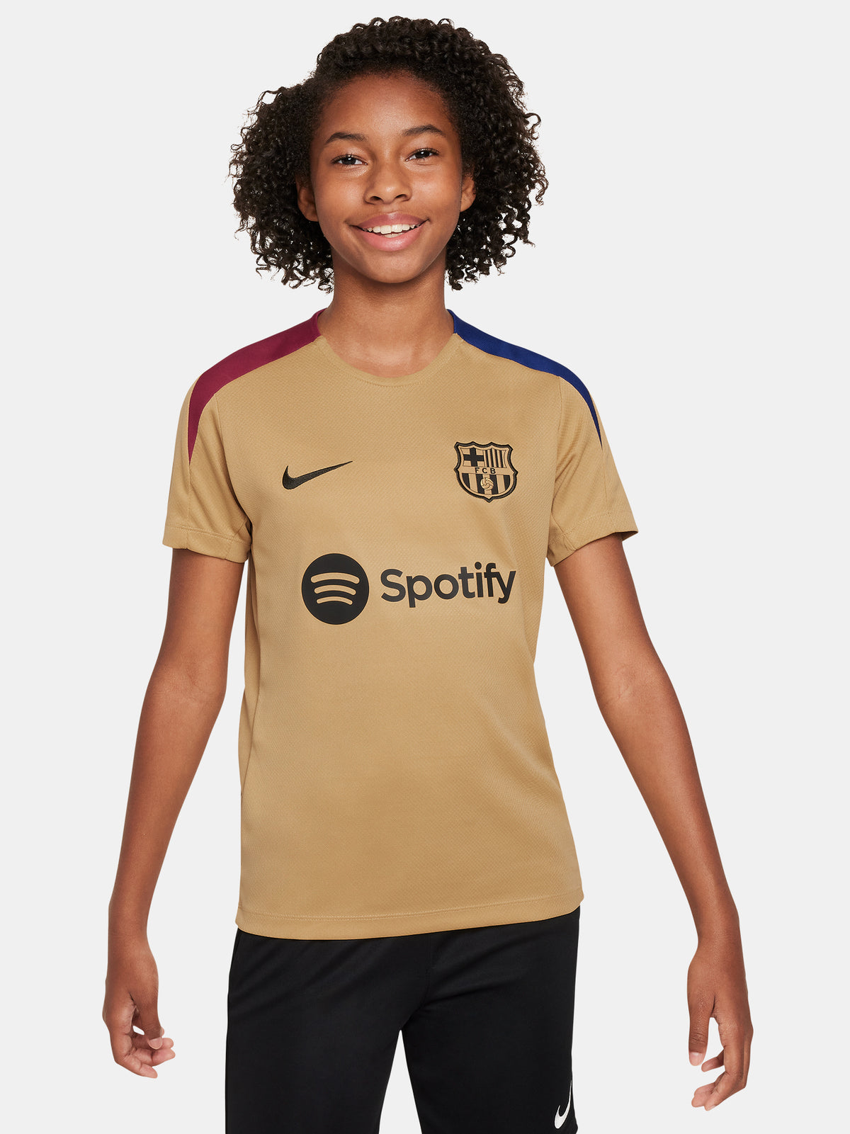 Child wearing an FC Barcelona gold training shirt with short sleeves, red and blue shoulder accents, Nike logo, and Spotify sponsor logo on the chest.




