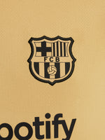 Two children wearing FC Barcelona gold training kits with short sleeves, featuring red and blue shoulder stripes, Nike logos, and Spotify sponsor branding.