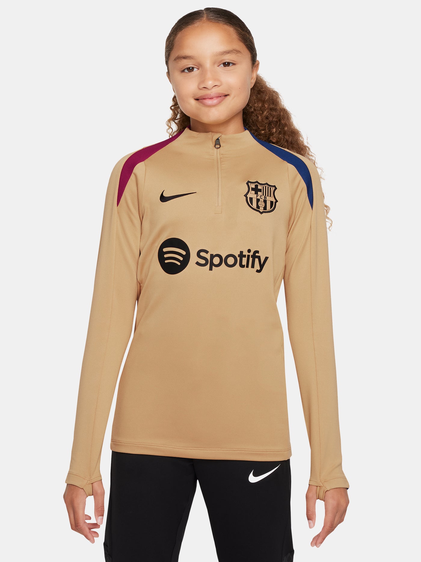 Girl wearing a long-sleeve FC Barcelona gold training top with a quarter-zip, red and blue shoulder accents, Nike logo, and Spotify sponsor logo.