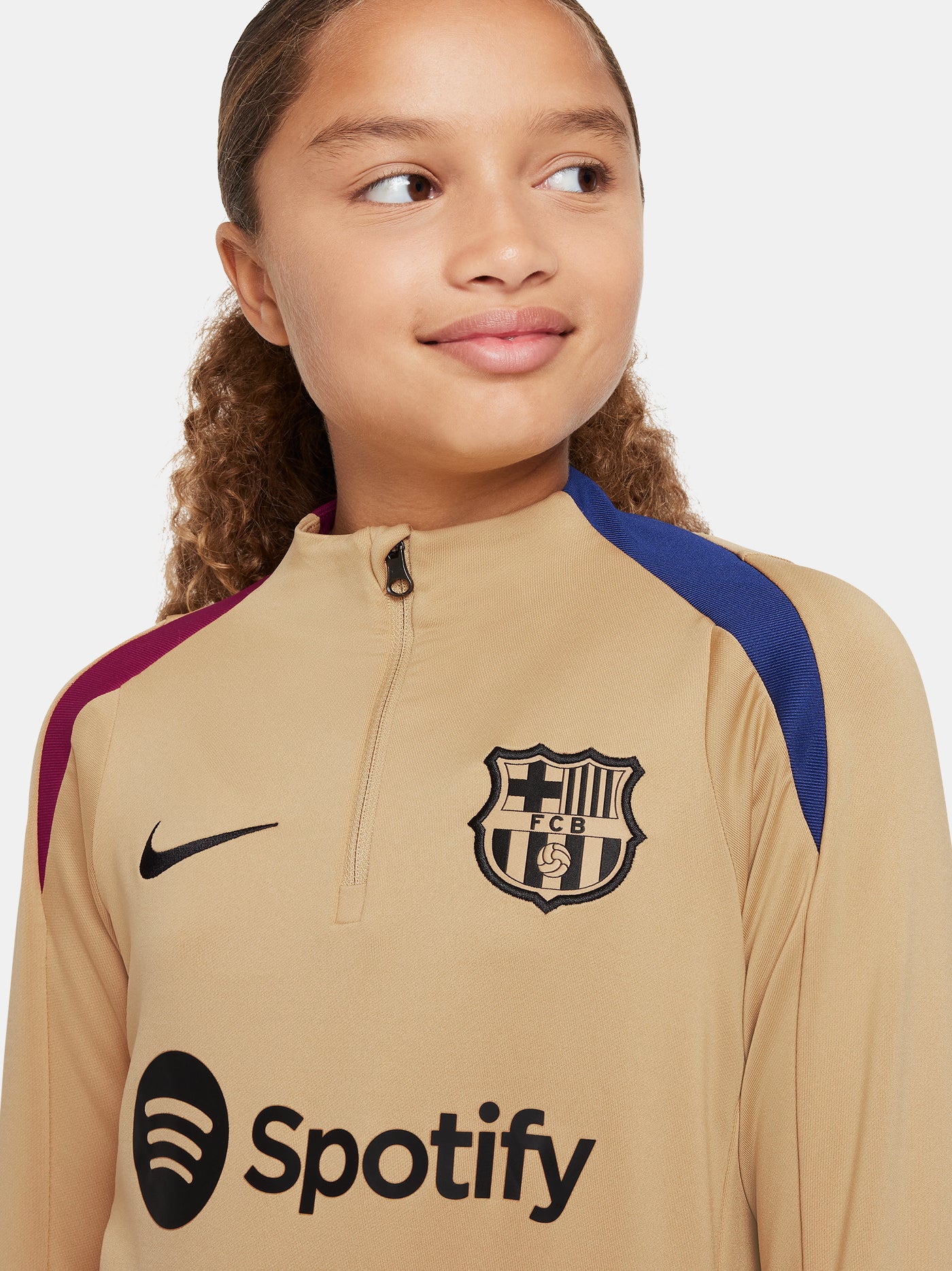 Girl wearing a long-sleeve FC Barcelona gold training top with a quarter-zip, red and blue shoulder accents, Nike logo, and Spotify sponsor logo.
