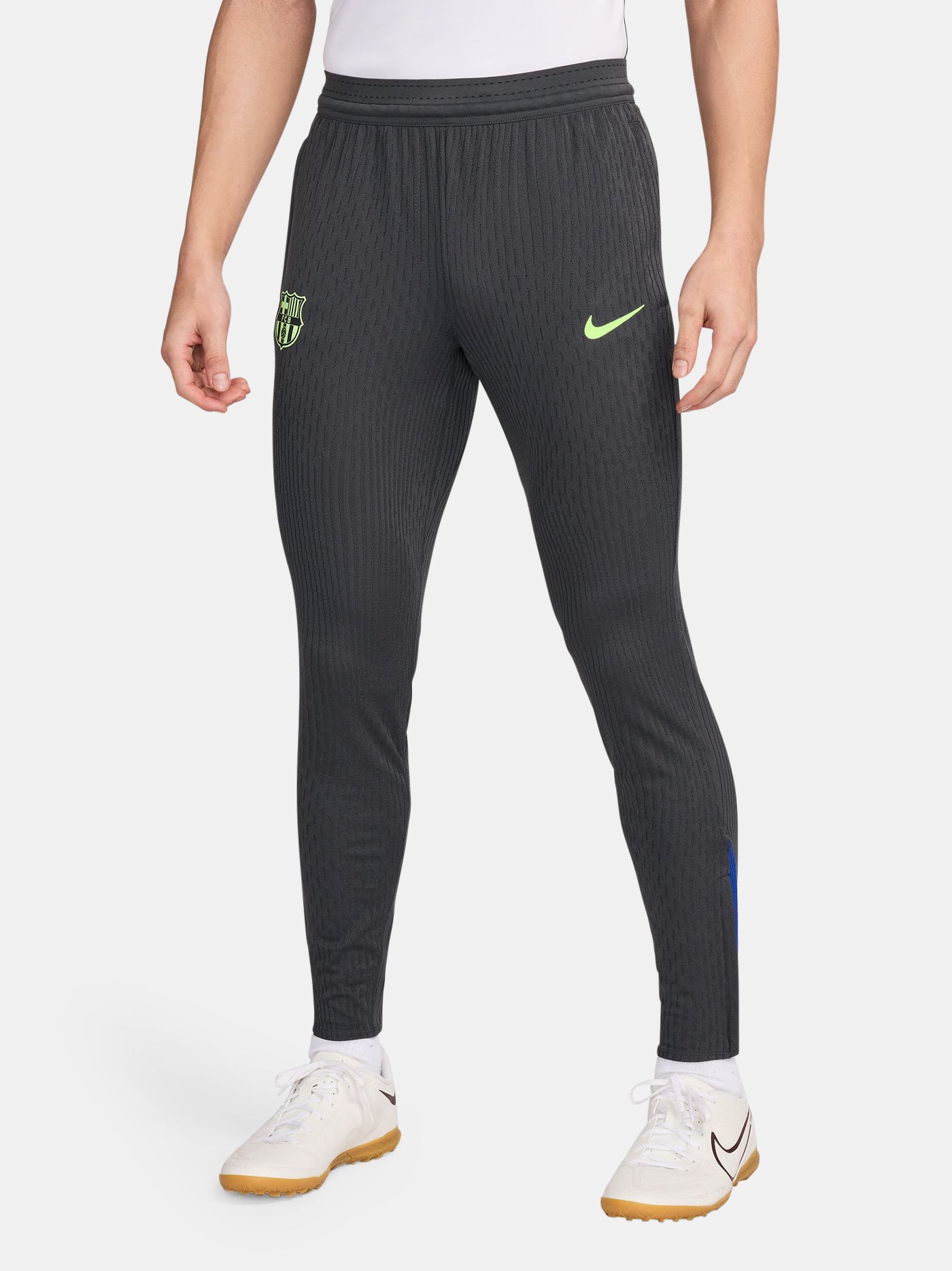 FC Barcelona dark grey tapered training pants with a subtle striped pattern, featuring a neon green Nike logo on the right thigh and the FC Barcelona crest in neon green on the left thigh.