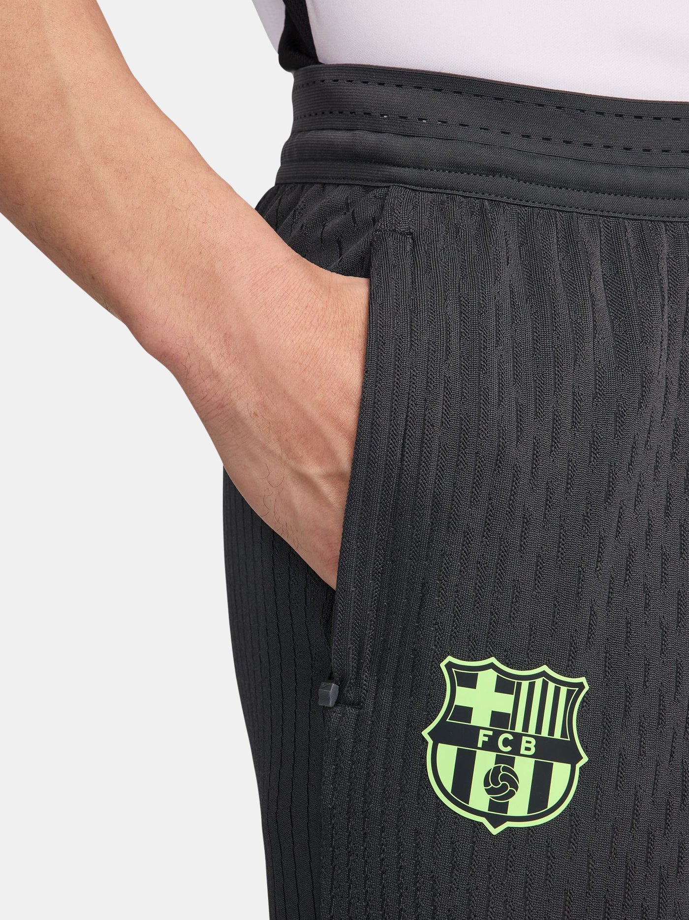 FC Barcelona dark grey tapered training pants with a subtle striped pattern, featuring a neon green Nike logo on the right thigh and the FC Barcelona crest in neon green on the left thigh.