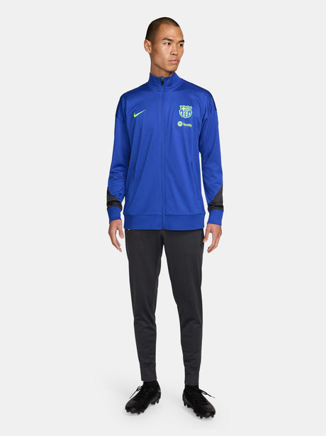 FC Barcelona blue full-zip training jacket featuring neon green Nike logo on the right chest and the FC Barcelona crest with Spotify sponsor on the left chest. Black accents on the lower sleeves. Paired with black training pants.