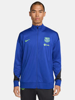 FC Barcelona blue full-zip training jacket featuring neon green Nike logo on the right chest and the FC Barcelona crest with Spotify sponsor on the left chest. Black accents on the lower sleeves. Paired with black training pants.