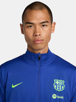 FC Barcelona blue full-zip training jacket featuring neon green Nike logo on the right chest and the FC Barcelona crest with Spotify sponsor on the left chest. Black accents on the lower sleeves. Paired with black training pants.