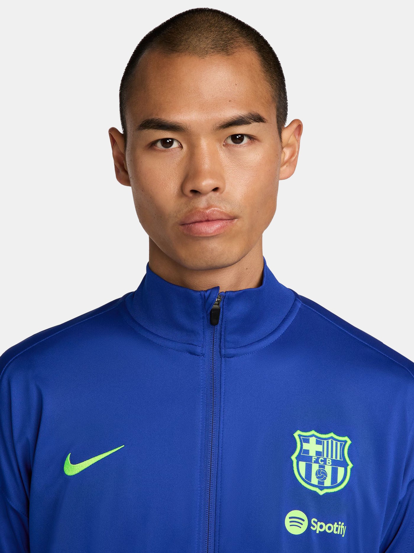 FC Barcelona blue full-zip training jacket featuring neon green Nike logo on the right chest and the FC Barcelona crest with Spotify sponsor on the left chest. Black accents on the lower sleeves. Paired with black training pants.