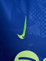 Women's FC Barcelona blue training jersey with neon green logos and side details.
