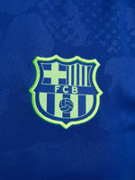 Women's FC Barcelona blue training jersey with neon green logos and side details.