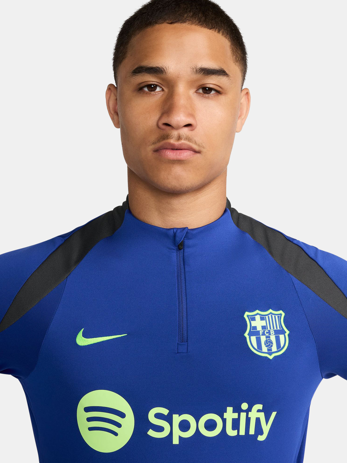 Men's FC Barcelona training kit consisting of a blue long-sleeve top with neon green Nike, Spotify, and club logos, paired with black training pants featuring matching neon green branding.