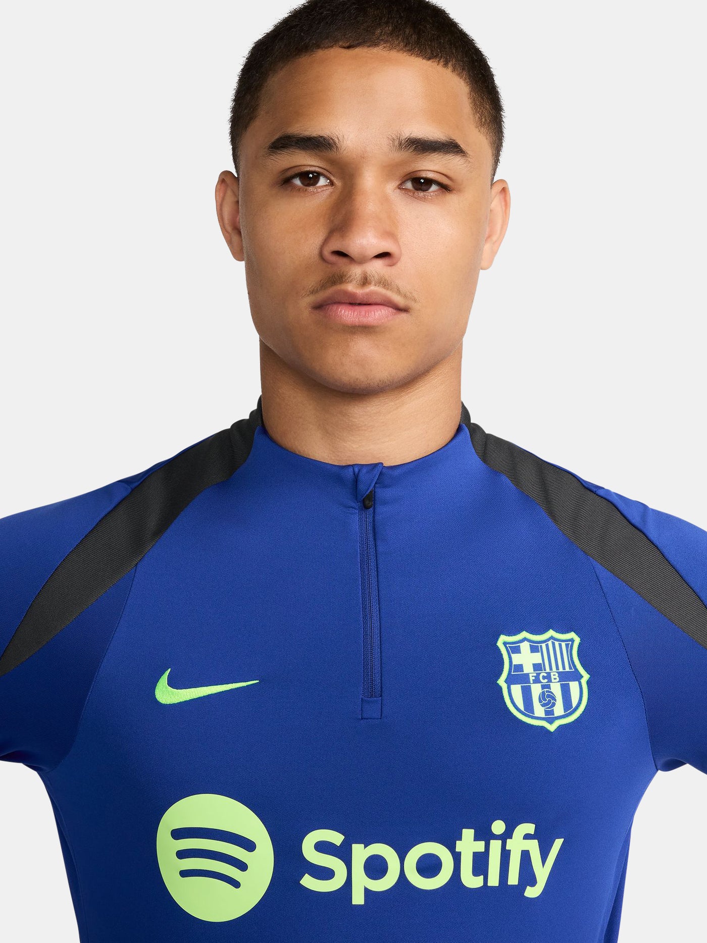 Men's FC Barcelona training kit consisting of a blue long-sleeve top with neon green Nike, Spotify, and club logos, paired with black training pants featuring matching neon green branding.