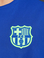 Blue FC Barcelona training jersey with neon green logos and black shoulder panels.