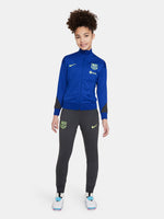 Women's FC Barcelona tracksuit featuring a blue zip-up jacket with neon green Nike and club logos, and dark grey pants with matching neon green details.







