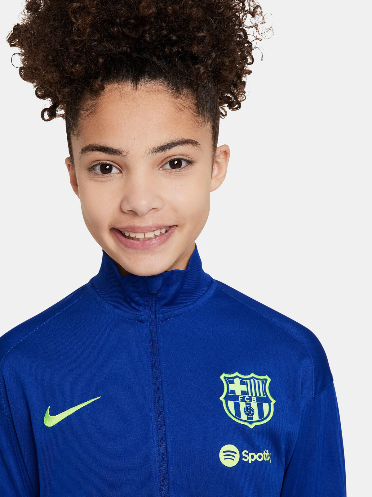 Women's FC Barcelona tracksuit featuring a blue zip-up jacket with neon green Nike and club logos, and dark grey pants with matching neon green details.




