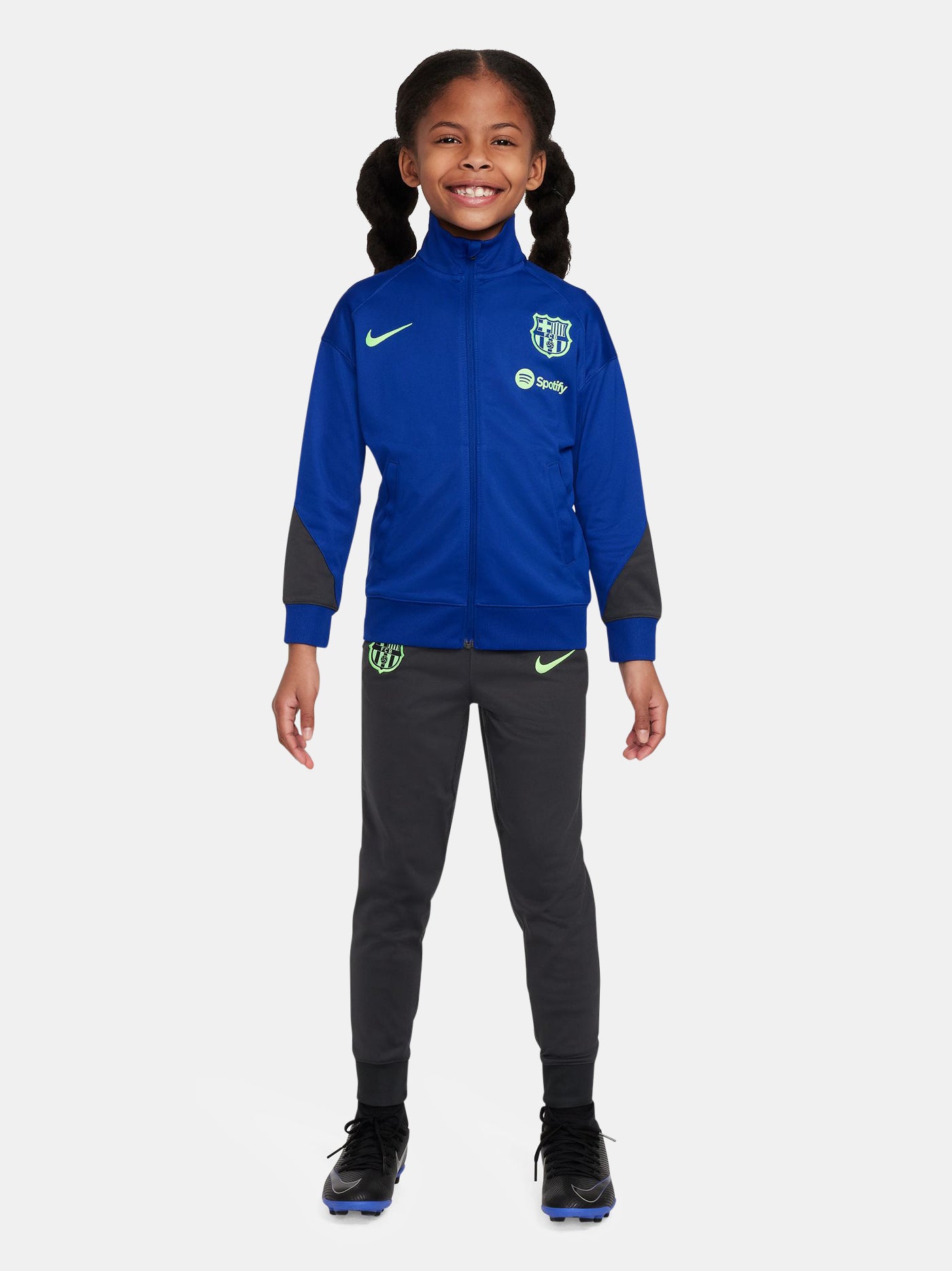 Kids' FC Barcelona tracksuit with blue jacket and black pants, featuring neon green crest and Nike logos.