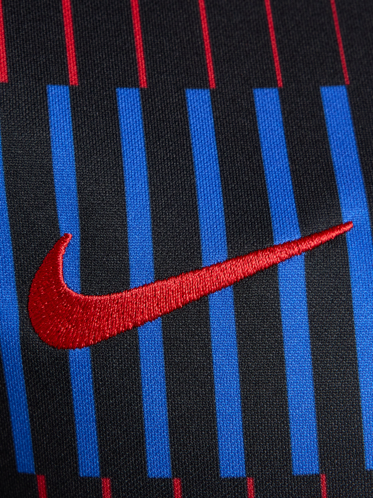FC Barcelona warm-up shirt featuring a black base with a striking vertical stripe pattern in alternating red and blue. The shirt displays the red Spotify logo in the center, along with the Nike swoosh and FC Barcelona crest, also in red.