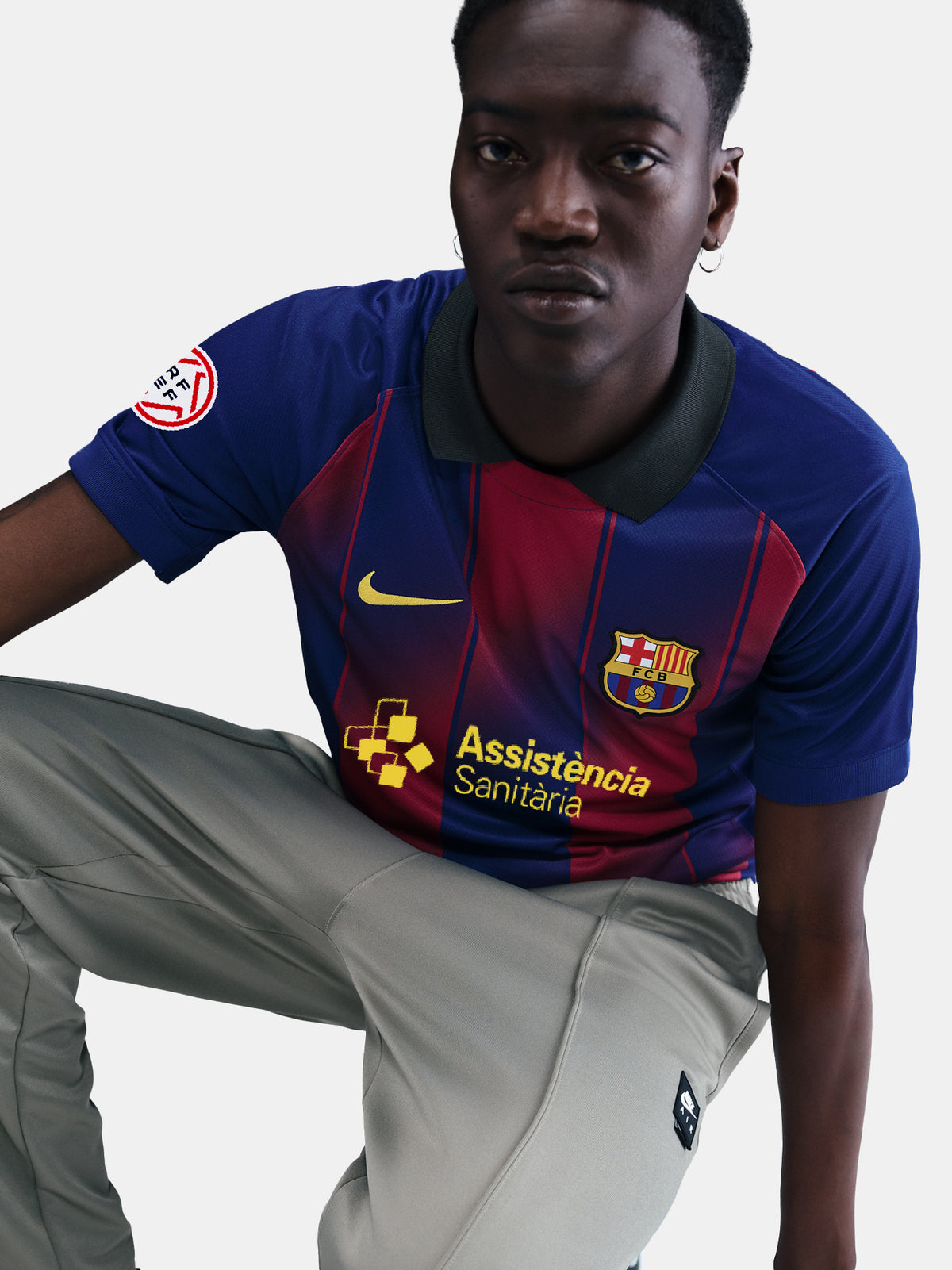 Man wearing the FC Barcelona home jersey in blue and red vertical stripes with black collar, featuring the Nike logo, club crest, and Assistència Sanitària sponsor.