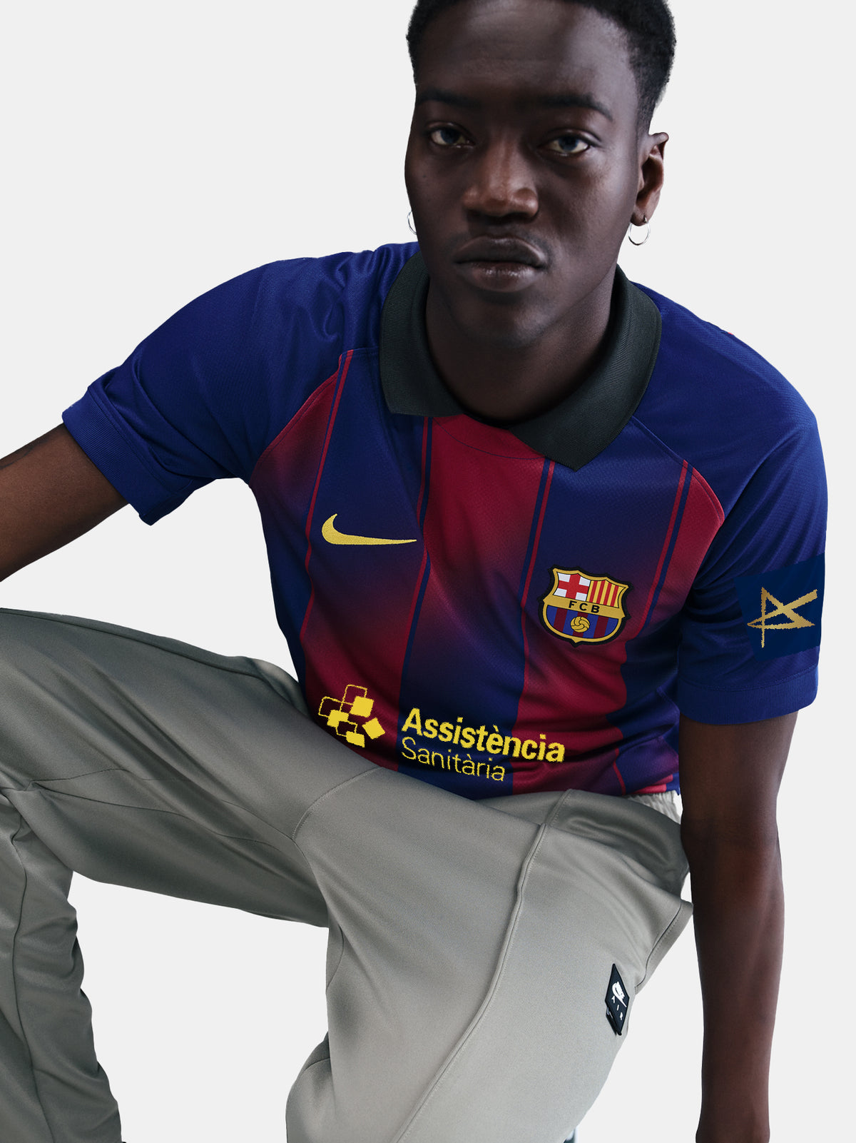 Man wearing the FC Barcelona home jersey in blue and red vertical stripes with black collar, featuring the Nike logo, club crest, and Assistència Sanitària sponsor.