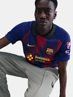 Man wearing the FC Barcelona home jersey in blue and red vertical stripes with black collar, featuring the Nike logo, club crest, and Assistència Sanitària sponsor.