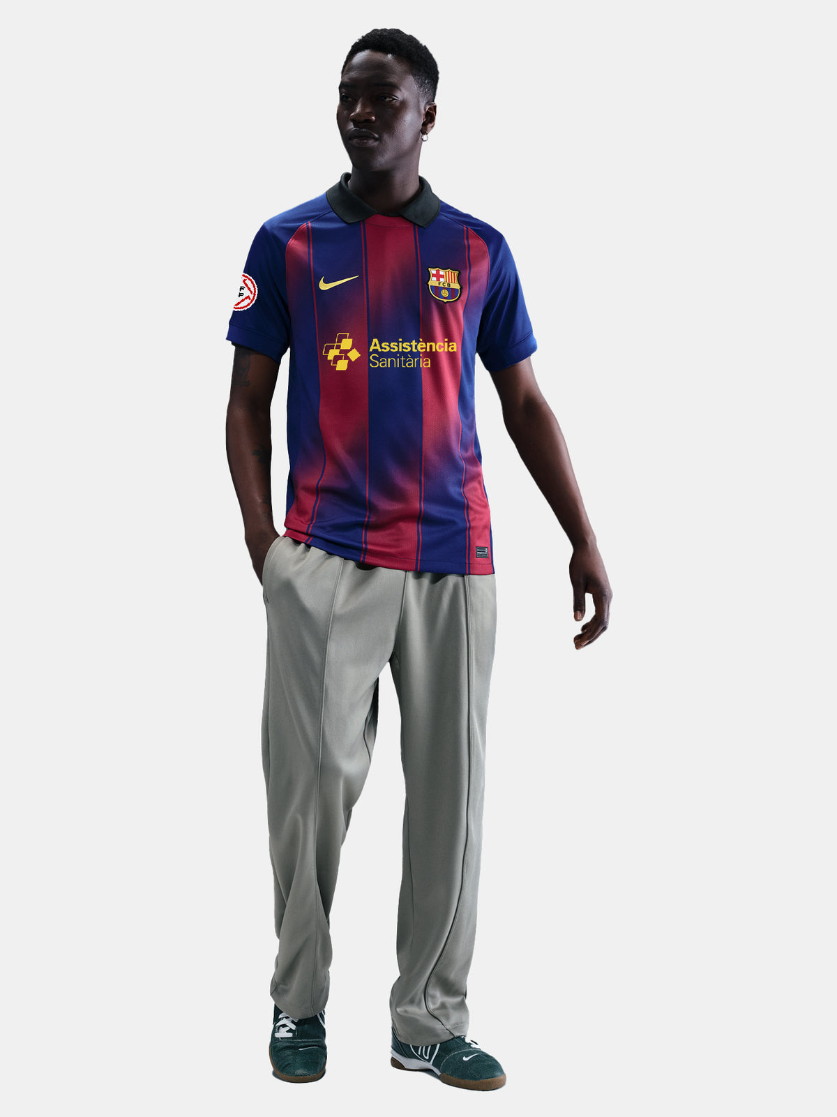 Man wearing the FC Barcelona home jersey in blue and red vertical stripes with black collar, featuring the Nike logo, club crest, and Assistència Sanitària sponsor.