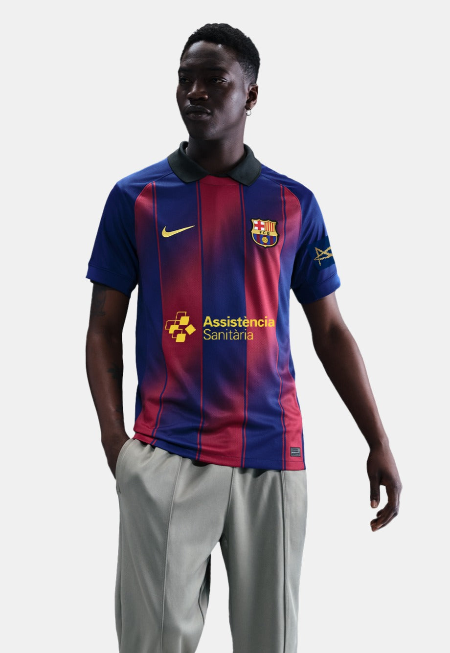 Man wearing the FC Barcelona home jersey in blue and red vertical stripes with black collar, featuring the Nike logo, club crest, and Assistència Sanitària sponsor.