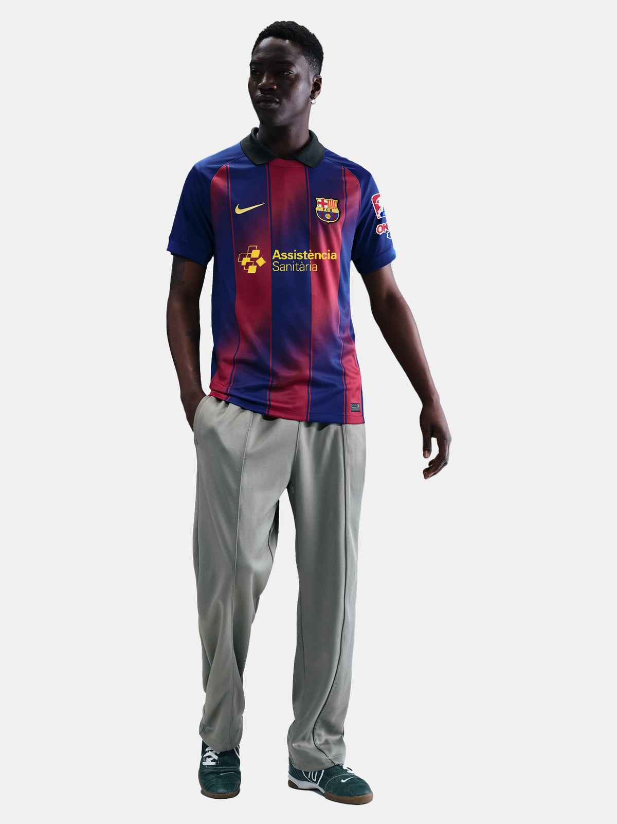 Man wearing the FC Barcelona home jersey in blue and red vertical stripes with black collar, featuring the Nike logo, club crest, and Assistència Sanitària sponsor.