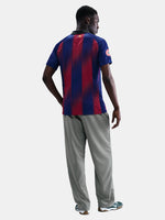 Man wearing the FC Barcelona home jersey in blue and red vertical stripes with black collar, featuring the Nike logo, club crest, and Assistència Sanitària sponsor.