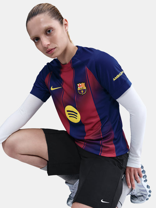 Person sitting with one leg up, wearing the FC Barcelona home jersey with red and blue stripes, yellow Nike and Spotify logos, and the "AMBILIGHT" patch on the sleeve. The image is cropped to show only the torso and part of the legs.
