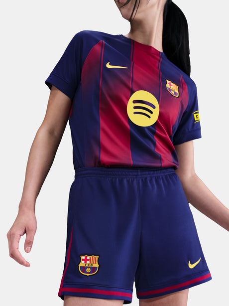 Close-up shot of navy blue shorts with red details and embroidered FC Barcelona and Nike logos, worn by a standing person against a white background.
