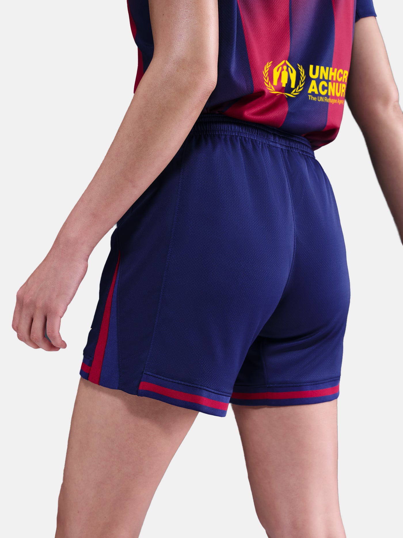 Close-up shot of navy blue shorts with red details and embroidered FC Barcelona and Nike logos, worn by a standing person against a white background.
