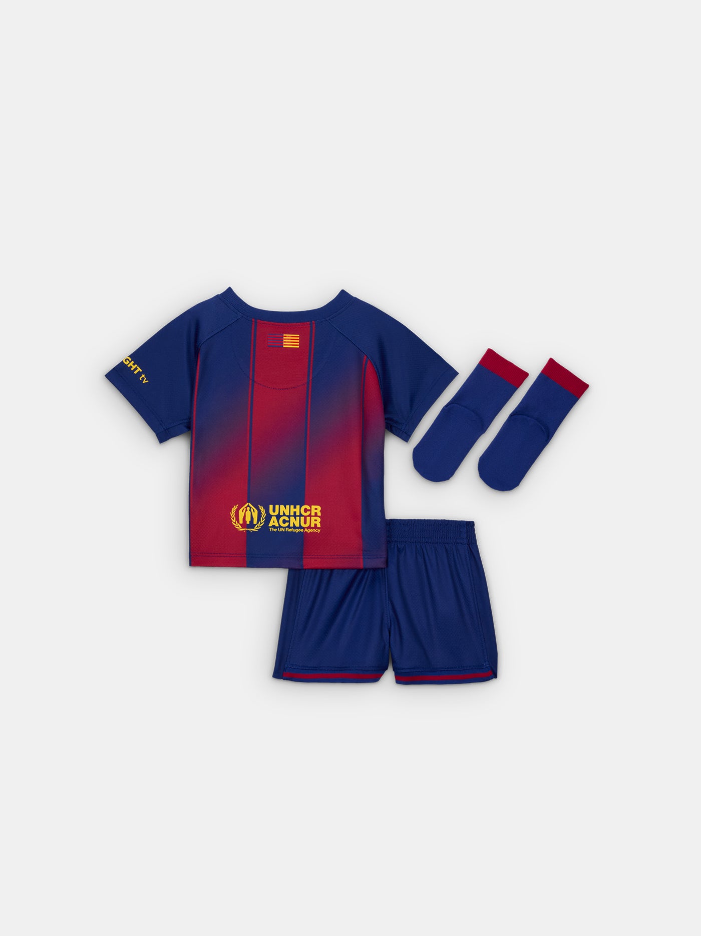 Flat lay of a Baby sized FC Barcelona home kit, including a red and blue striped jersey with Nike and Spotify logos, matching shorts with the Barça crest, and blue socks with red tops and yellow Nike swooshes.
